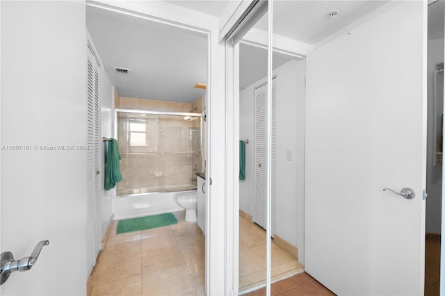 bathroom featuring tile patterned flooring, enclosed tub / shower combo, and toilet