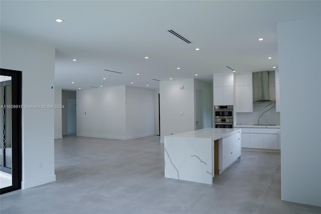 kitchen with white cabinets, light stone counters, wall chimney exhaust hood, a center island, and stainless steel double oven