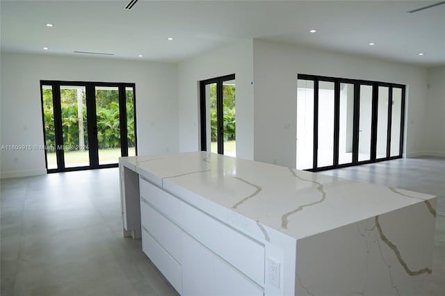 kitchen with light stone countertops, french doors, white cabinetry, and a kitchen island