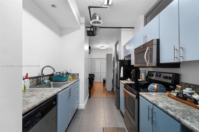 kitchen with stainless steel appliances, sink, blue cabinetry, and dark tile flooring