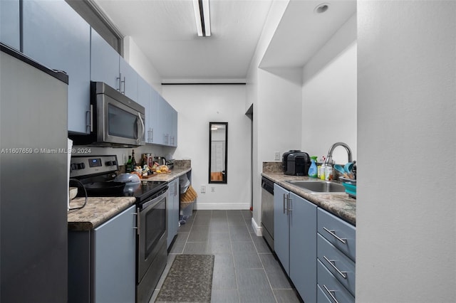 kitchen with blue cabinets, dark tile flooring, stainless steel appliances, and sink