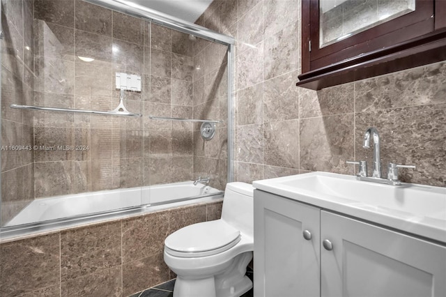 full bathroom featuring bath / shower combo with glass door, tile walls, vanity, and toilet