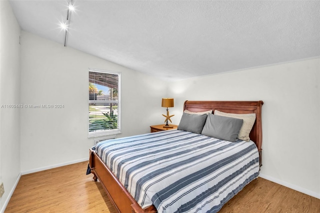 bedroom featuring lofted ceiling, light hardwood / wood-style flooring, and a textured ceiling