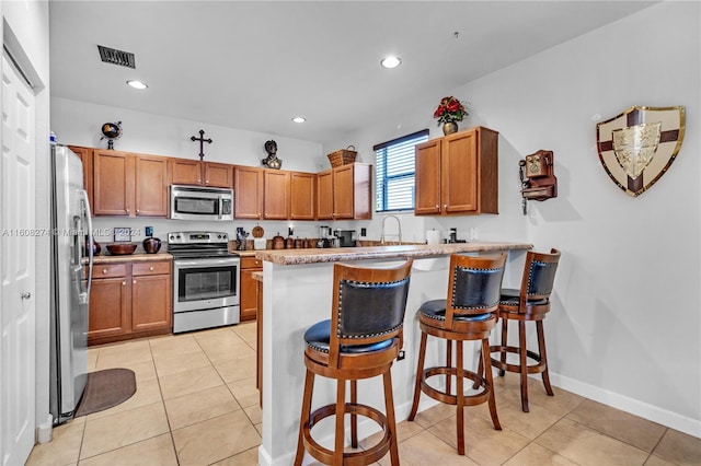 kitchen with light tile flooring, kitchen peninsula, stainless steel appliances, a breakfast bar area, and sink