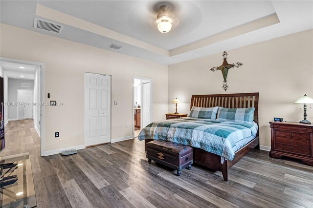 bedroom with a tray ceiling, hardwood / wood-style flooring, ceiling fan, and ensuite bath