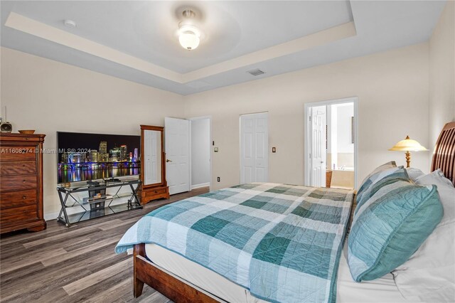 bedroom with ensuite bathroom, hardwood / wood-style flooring, and a raised ceiling