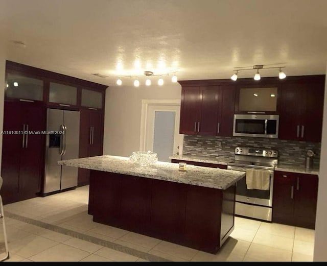 kitchen with light tile patterned floors, appliances with stainless steel finishes, a kitchen island, and glass insert cabinets