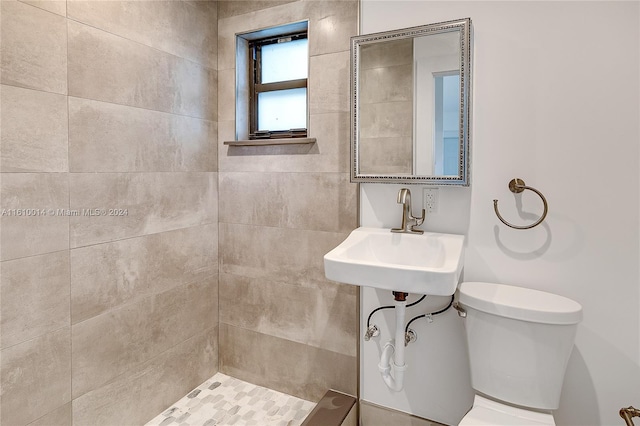 bathroom featuring a tile shower, sink, and toilet