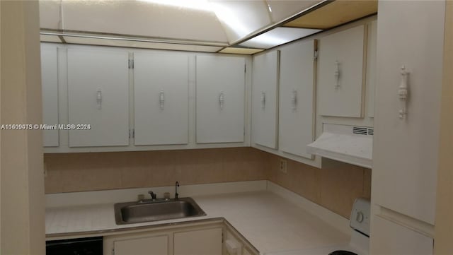 kitchen featuring light countertops, stove, white cabinets, a sink, and under cabinet range hood