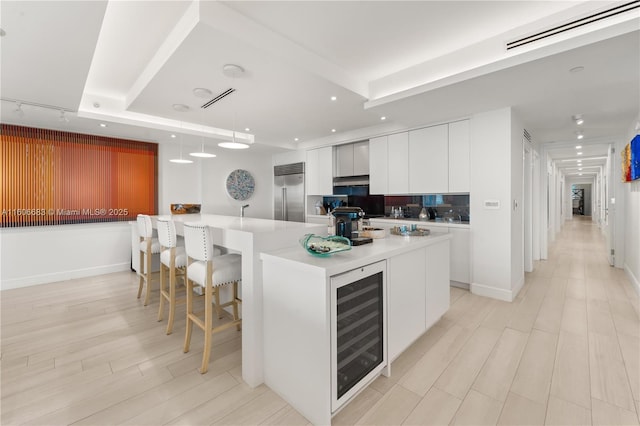 kitchen with stainless steel built in fridge, white cabinets, decorative light fixtures, beverage cooler, and a tray ceiling