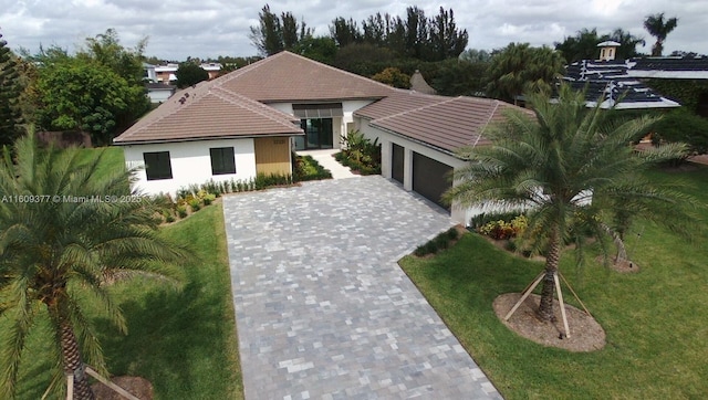 view of front of property featuring a front yard, decorative driveway, a tile roof, and an attached garage