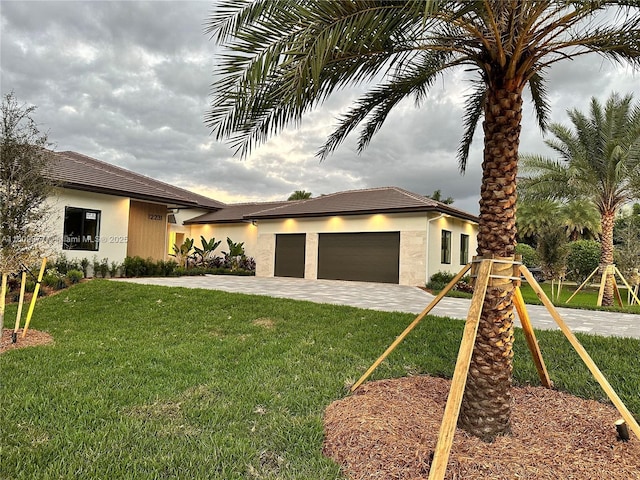 prairie-style house featuring a garage, driveway, a front yard, and stucco siding