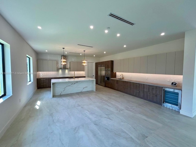 kitchen with decorative backsplash, light stone counters, stainless steel appliances, a spacious island, and sink