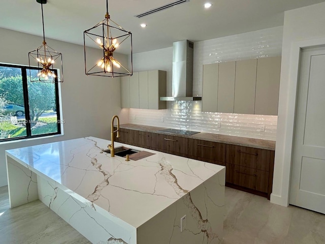 kitchen featuring light stone counters, wall chimney exhaust hood, sink, pendant lighting, and white cabinetry