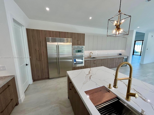 kitchen featuring light stone countertops, appliances with stainless steel finishes, sink, decorative light fixtures, and a notable chandelier