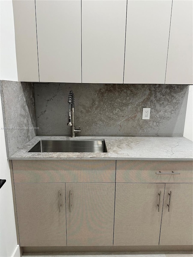 kitchen with backsplash, light stone counters, and sink