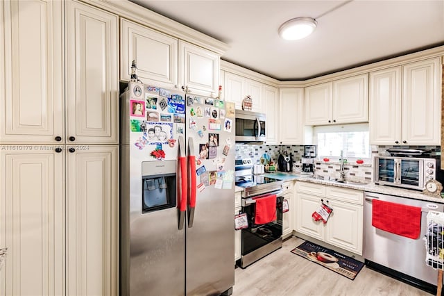 kitchen with sink, light hardwood / wood-style flooring, decorative backsplash, light stone countertops, and appliances with stainless steel finishes