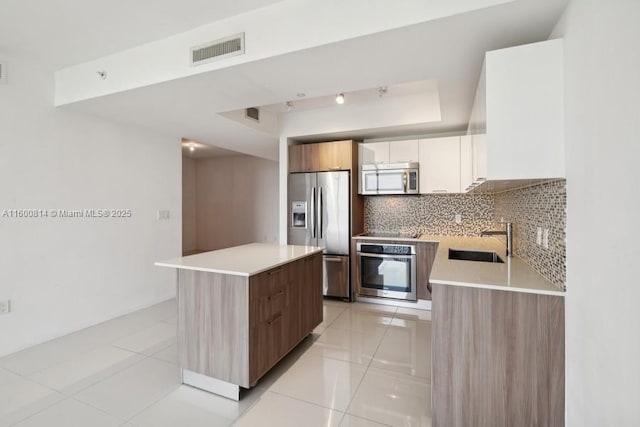 kitchen with a center island, a raised ceiling, sink, white cabinetry, and appliances with stainless steel finishes