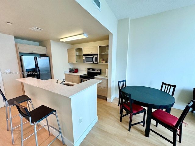 kitchen featuring sink, stainless steel appliances, a kitchen breakfast bar, and light brown cabinets