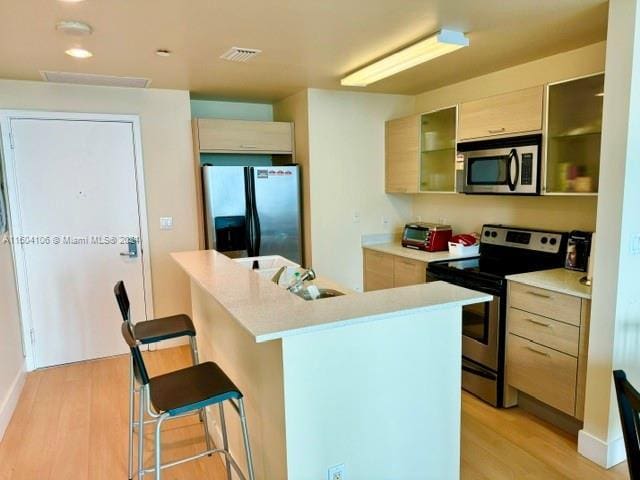 kitchen with stainless steel appliances, an island with sink, light wood-type flooring, a breakfast bar, and light brown cabinets