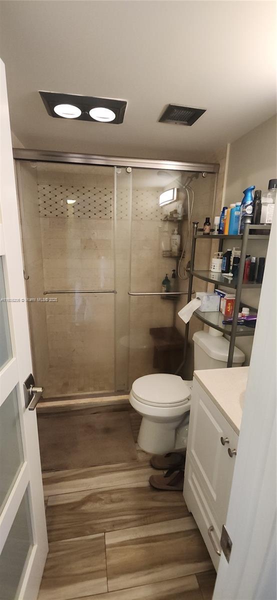 bathroom with hardwood / wood-style flooring, vanity, toilet, and walk in shower