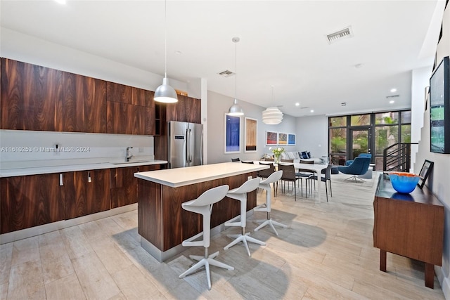 kitchen with stainless steel fridge, expansive windows, light hardwood / wood-style flooring, a kitchen island, and hanging light fixtures