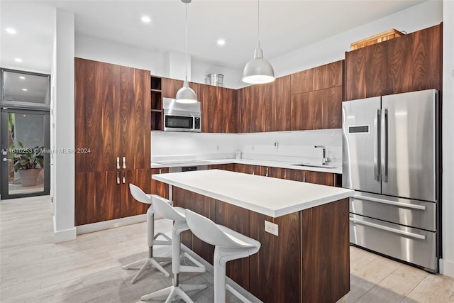 kitchen featuring pendant lighting, sink, light hardwood / wood-style floors, appliances with stainless steel finishes, and a kitchen island