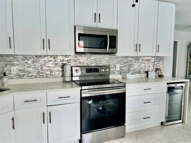 kitchen featuring beverage cooler, stainless steel appliances, light tile patterned flooring, backsplash, and white cabinets