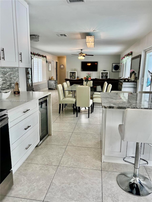 kitchen featuring ceiling fan, wine cooler, light stone counters, backsplash, and white cabinets