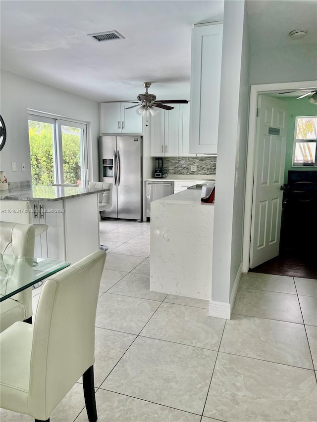 kitchen featuring stainless steel appliances, light tile patterned floors, tasteful backsplash, light stone counters, and white cabinets