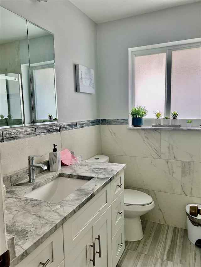 bathroom with vanity, toilet, and tile walls