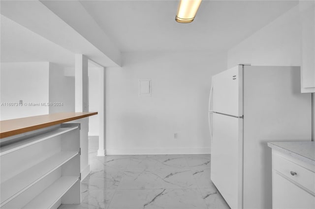 kitchen with white refrigerator, white cabinets, and light tile flooring