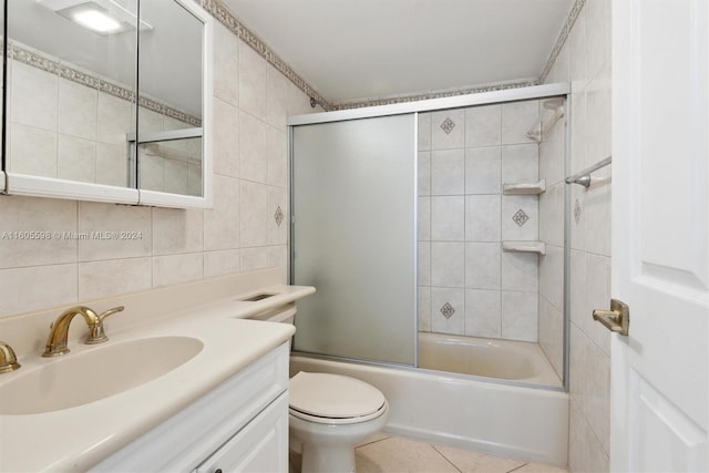 full bathroom with vanity, bath / shower combo with glass door, tile patterned flooring, toilet, and tile walls