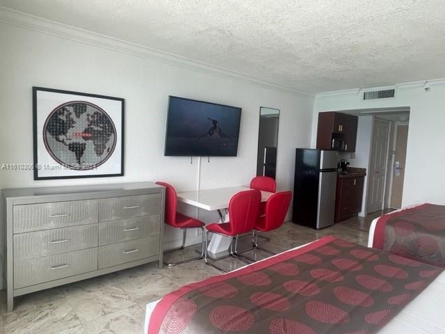 bedroom featuring stainless steel refrigerator, a textured ceiling, and ornamental molding