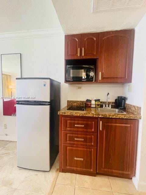 kitchen featuring white refrigerator, dark stone counters, ornamental molding, and sink