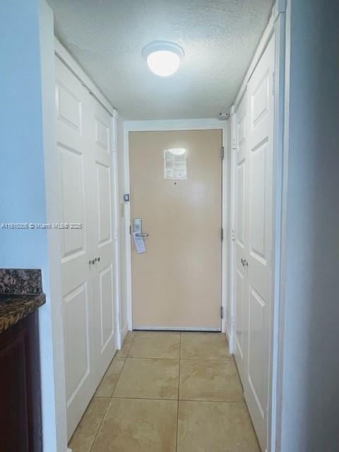 hallway with a textured ceiling and light tile patterned flooring