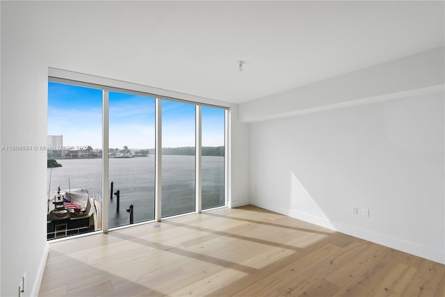 spare room featuring a water view, expansive windows, and light hardwood / wood-style flooring