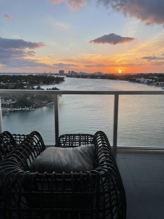 balcony at dusk featuring a water view