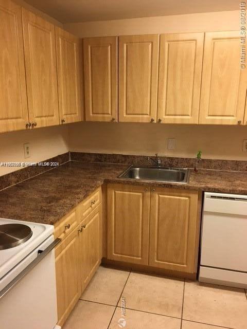 kitchen with white appliances, a sink, light tile patterned floors, dark countertops, and light brown cabinetry