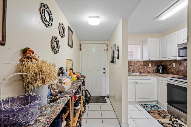 kitchen with white cabinets, sink, light tile patterned floors, a textured ceiling, and range