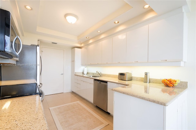 kitchen featuring white cabinets, light stone counters, appliances with stainless steel finishes, a tray ceiling, and sink