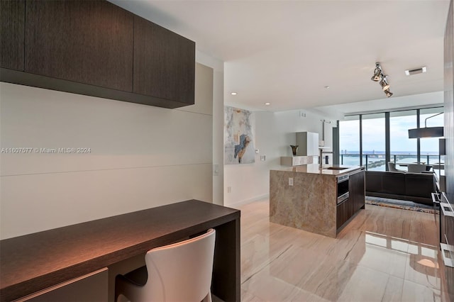 kitchen featuring dark brown cabinetry, sink, a water view, oven, and an island with sink