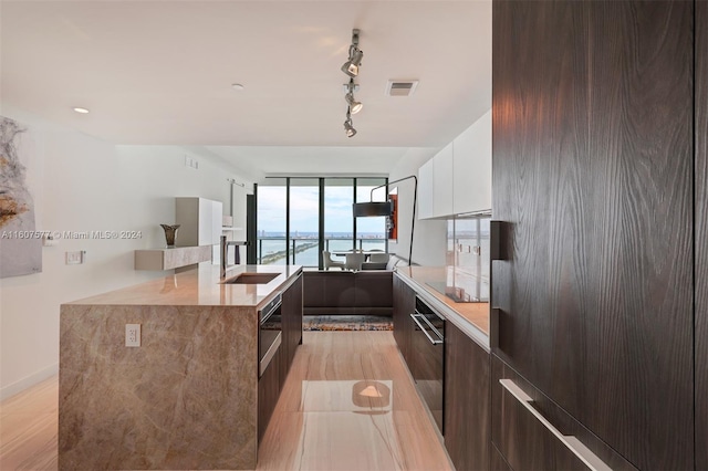 kitchen featuring black electric stovetop, a water view, sink, white cabinetry, and dark brown cabinetry