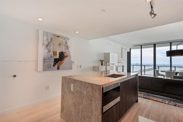 kitchen with dark brown cabinetry, sink, light hardwood / wood-style flooring, oven, and a water view