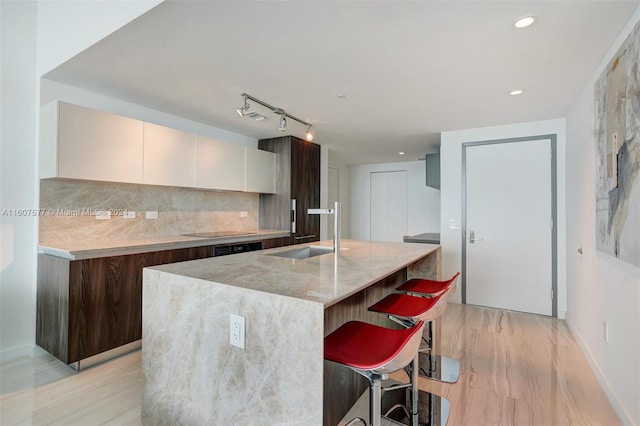 kitchen featuring light stone countertops, sink, tasteful backsplash, a breakfast bar, and white cabinets