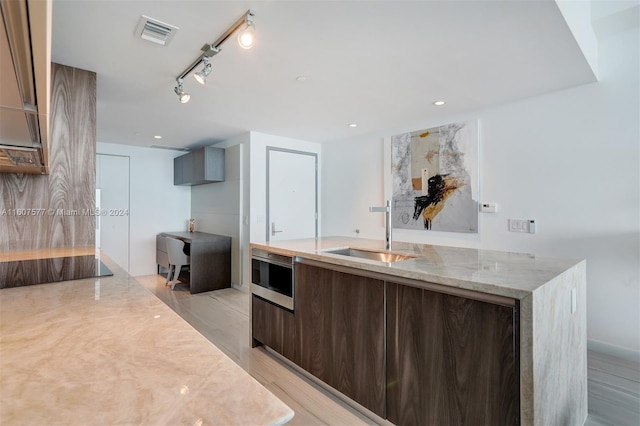 kitchen with light stone counters, sink, rail lighting, and light hardwood / wood-style floors