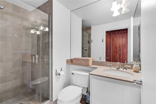 bathroom with vanity, an inviting chandelier, toilet, and a shower with door