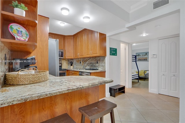 kitchen featuring tasteful backsplash, stainless steel appliances, light stone counters, light tile floors, and a breakfast bar area