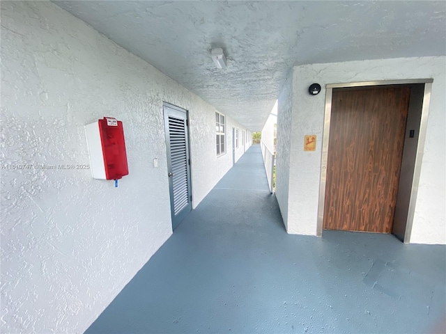 hall with concrete flooring and a textured wall