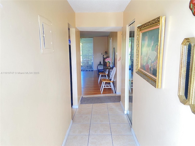 hallway with light tile patterned floors, electric panel, and baseboards